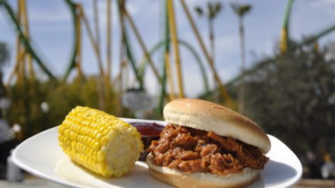 A BBQ brisket Sandwich with Corn on the Cob on a plate in front of The Riddler's Revenge