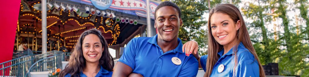 Three six flags employees standing together in front of a carousel