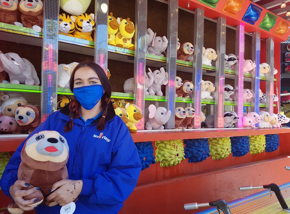 a masked employee holding a stuffed animal prize in a game at Six flags